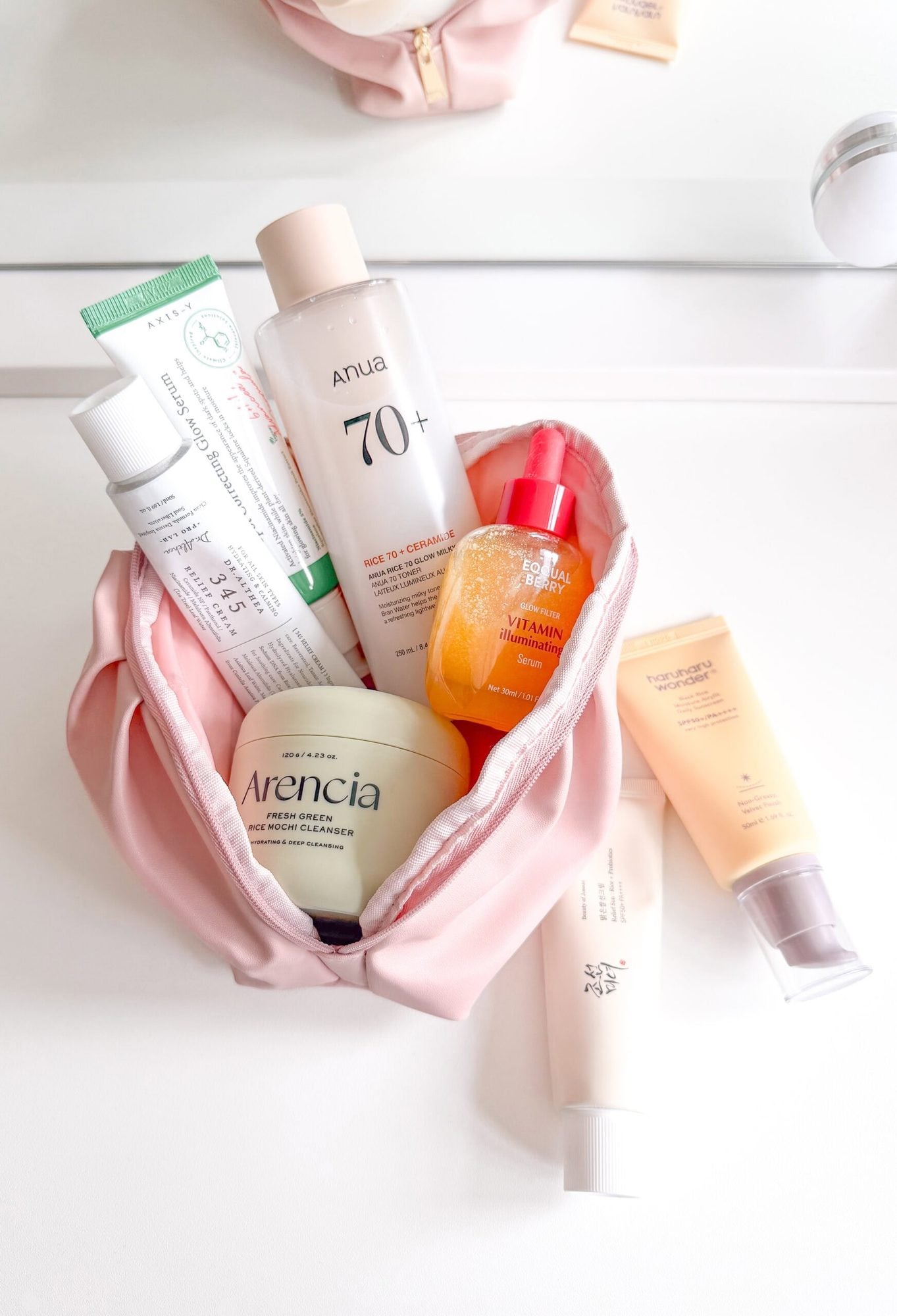 Skincare and serum products arranged in a pink cosmetic bag on white background