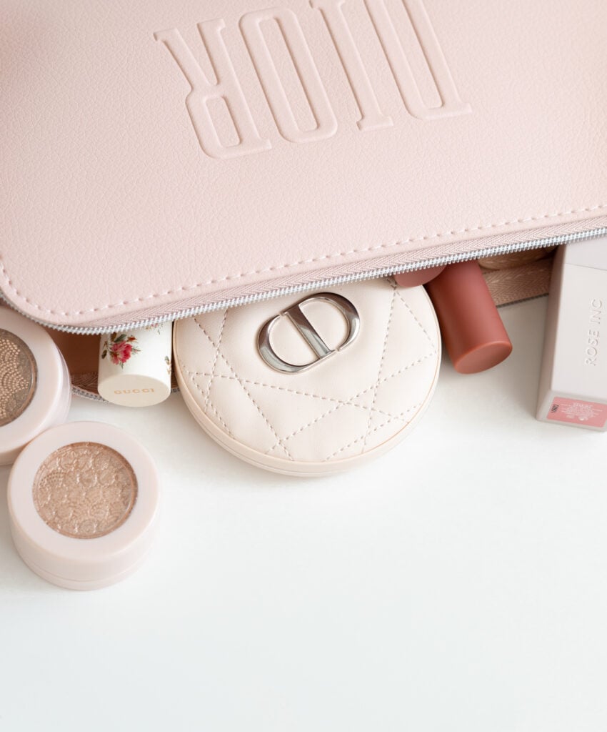 Pink quilted cosmetic pouch with makeup products including loose shimmer and cream products inside