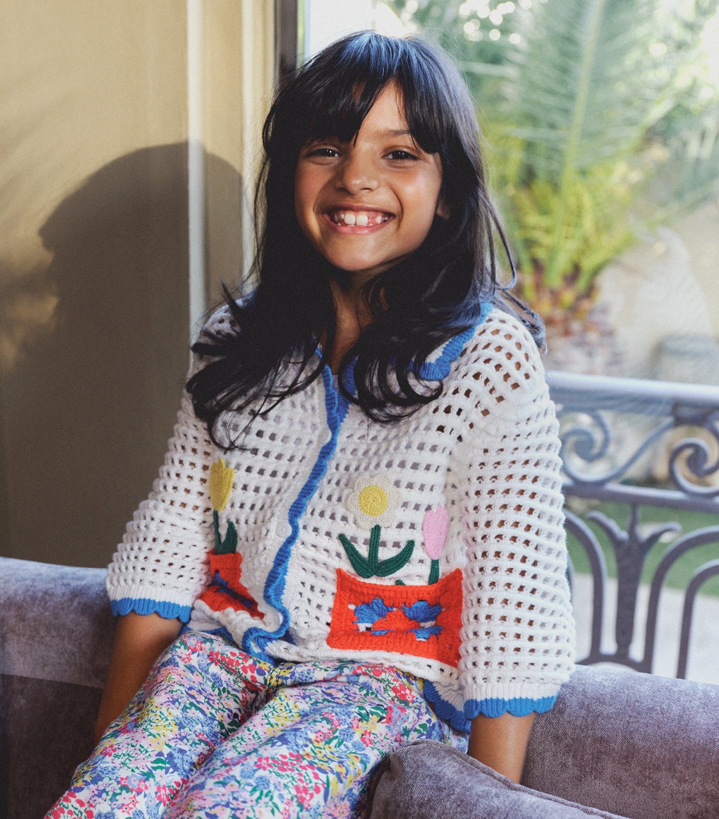 Young girl smiling wearing cream knit sweater with colorful cat design and floral pants