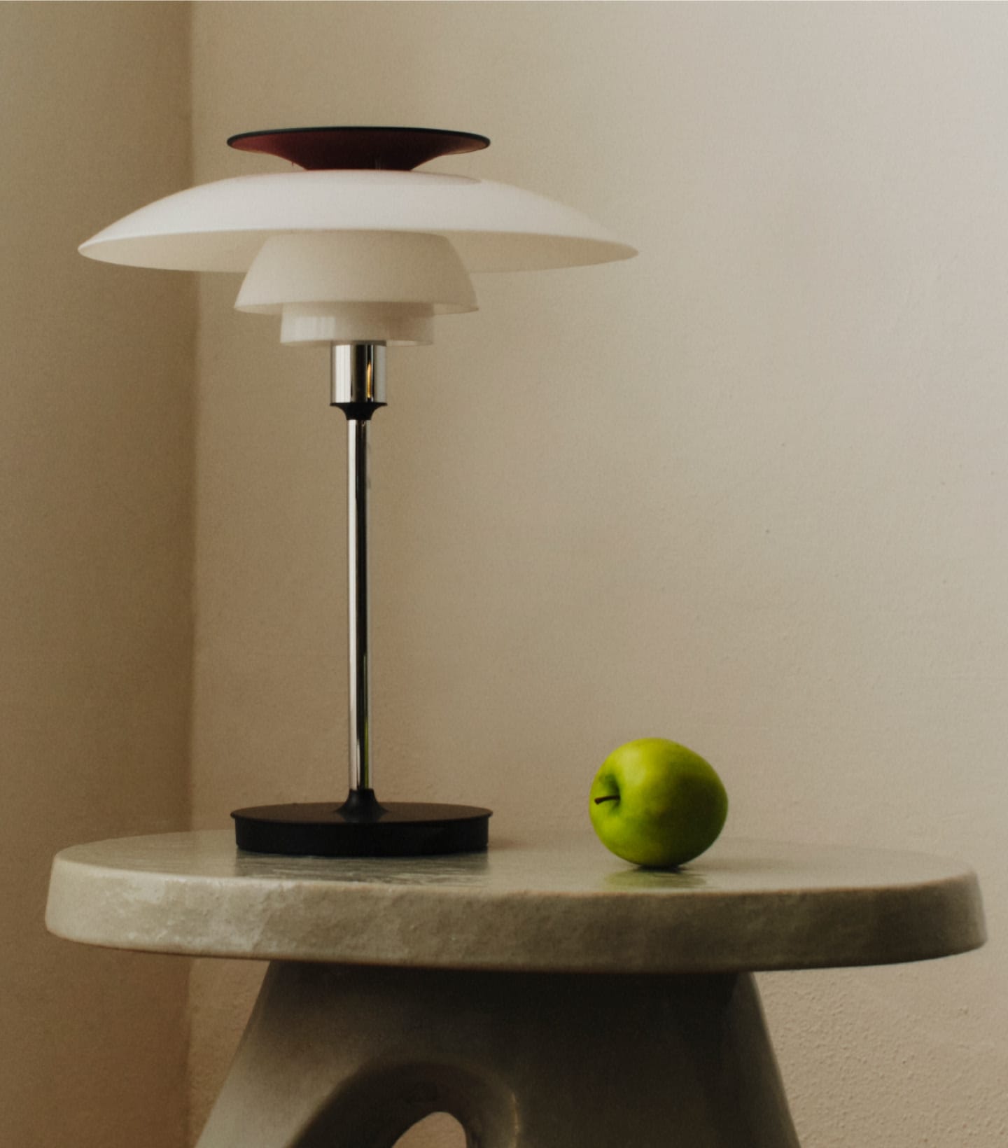 Minimalist table lamp with layered white shade next to green apple on round stone table