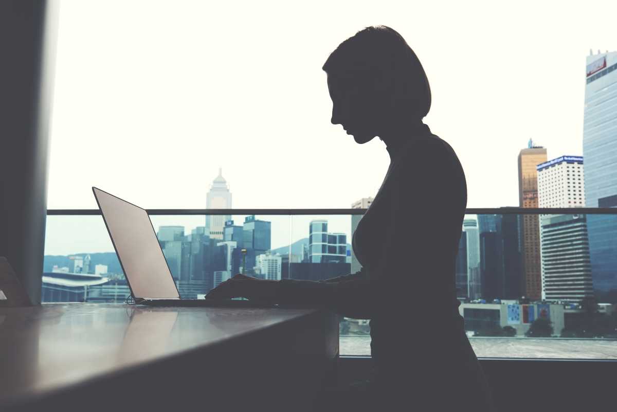 Silhouette of a person working at a laptop on a high-rise office balcony with city skyline view